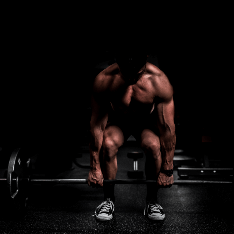 Male bodybuilder lifting bar in dark background